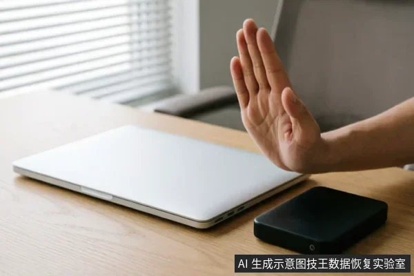 木质桌面上放置着一台闭合的银色笔记本电脑和一个黑色移动硬盘。画面右侧伸出一只手掌,掌心向外对着设备做出明确的“停止”或“拒绝”手势,示意不要连接或使用该存储设备。