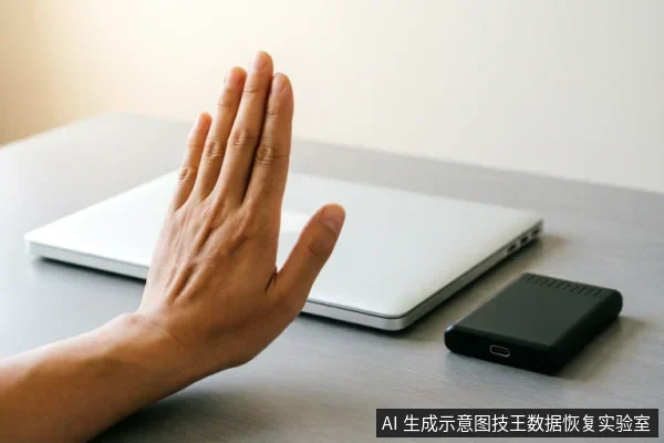 一只手掌在闭合的银色笔记本电脑前做出停止手势,旁边放置着一个黑色的移动硬盘。画面直观地传达了在数据恢复或硬件故障排查初期,应立即停止写入操作、避免盲目通电或继续使用的警示含义。