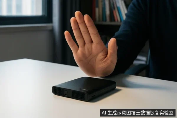 白色桌面上放着一台黑色移动硬盘，一只手掌在硬盘上方做出停止手势，背景为书架和窗户。
